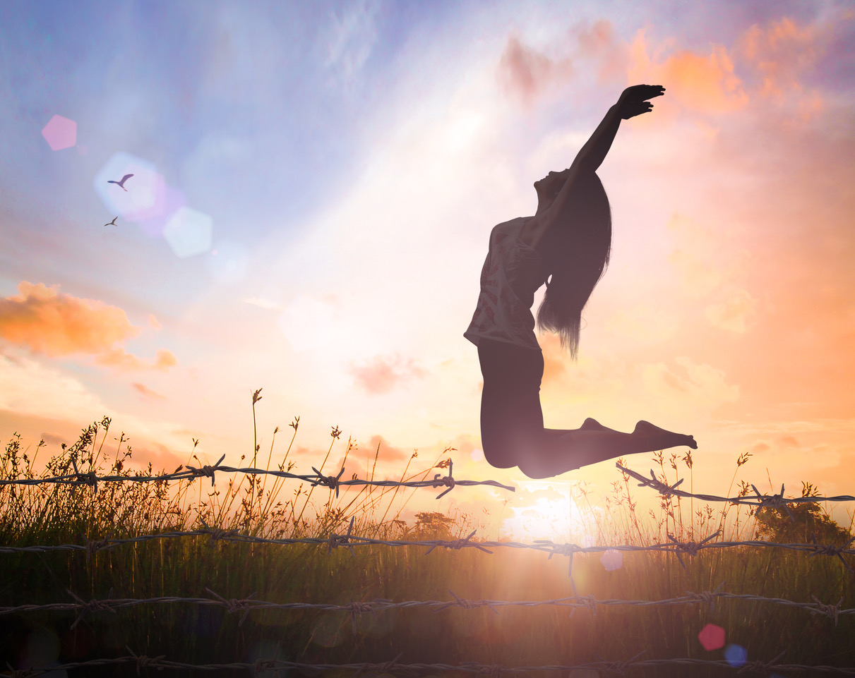 International human rights day concept: Silhouette of a girl jumping over broken barbed wire at autumn sunset meadow with her hands raised